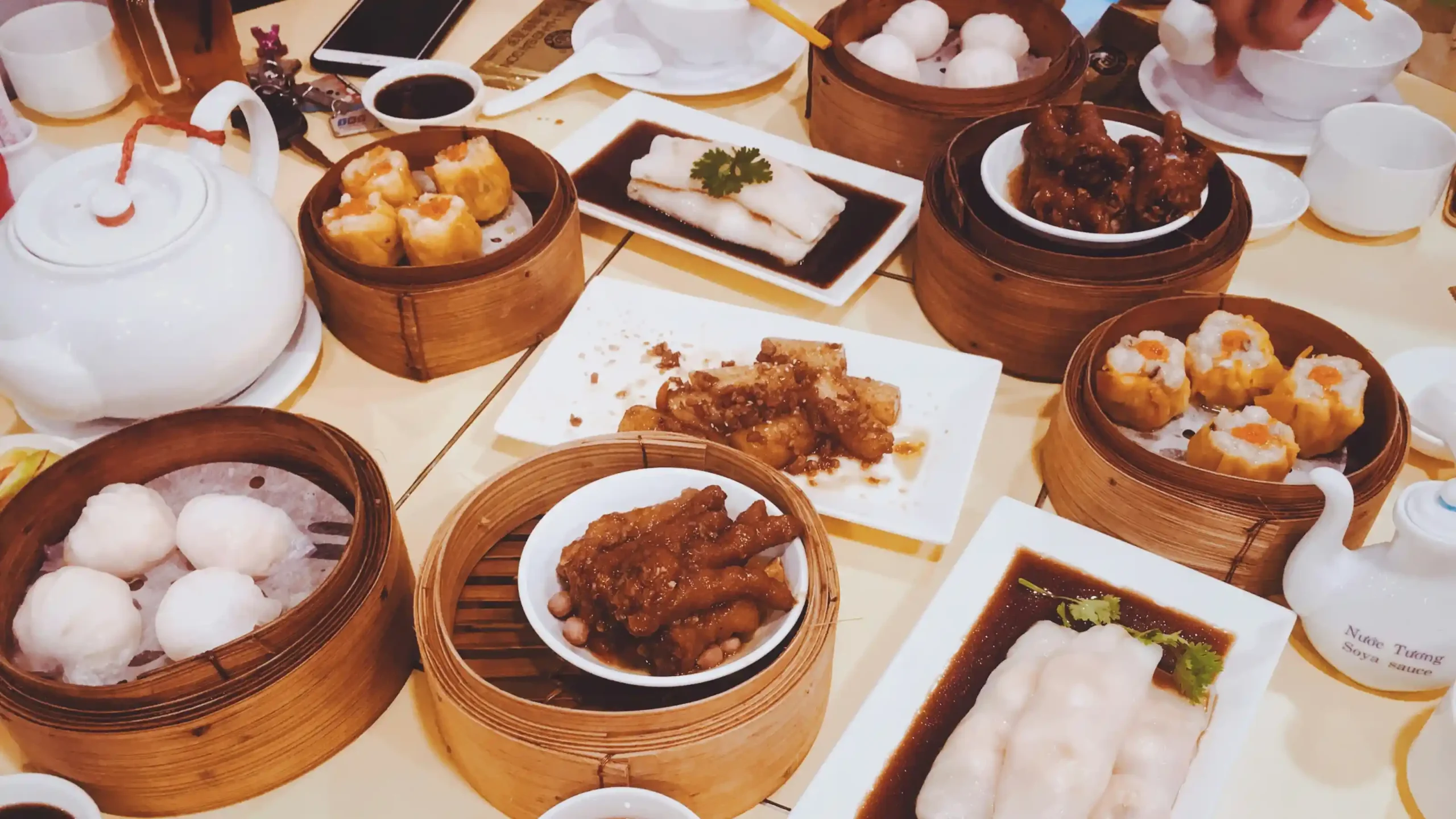中式点心餐桌上摆放烧卖、肠粉、蒸排骨及其他传统点心,多种竹制蒸笼与茶具展示中式餐饮丰富的菜品组合和堂食文化。