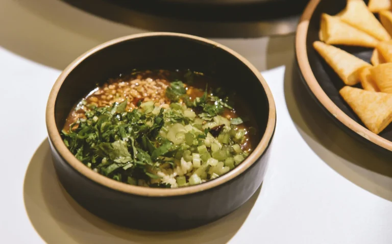 A small bowl of hot pot dipping sauce, primarily made with sesame oil, minced garlic, chopped green onions, and cilantro