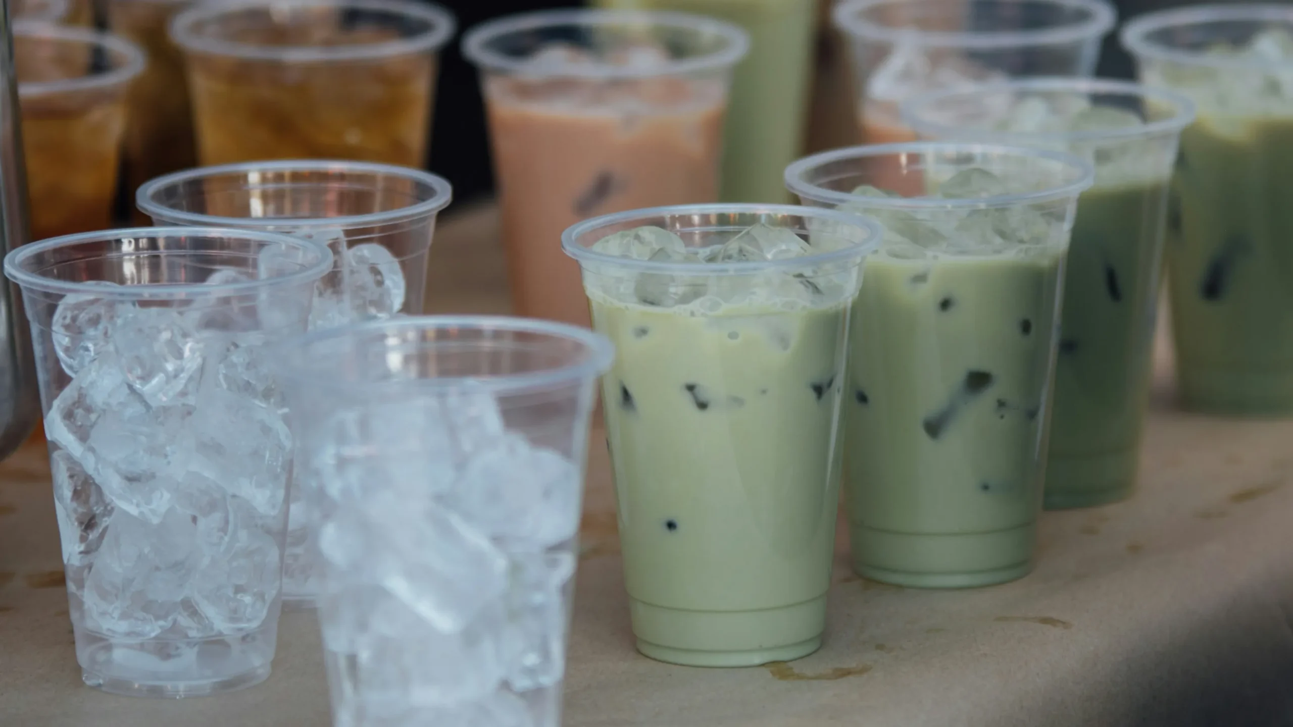 桌面上放置着不同风味的冰奶茶,绿色的是绿茶奶茶,红色的是草莓奶茶。