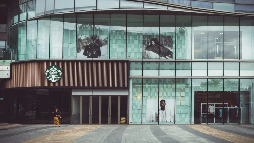 开在商场一楼的星巴克店铺外景,玻璃幕墙上有多个广告海报,展示时尚人物,环境现代化。