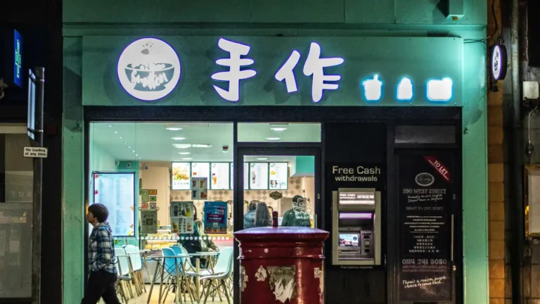 这是一家位于美国的手作中餐馆的外景，店铺招牌上写着“手作”，店内明亮，顾客正在用餐。餐馆门前有路人行走。