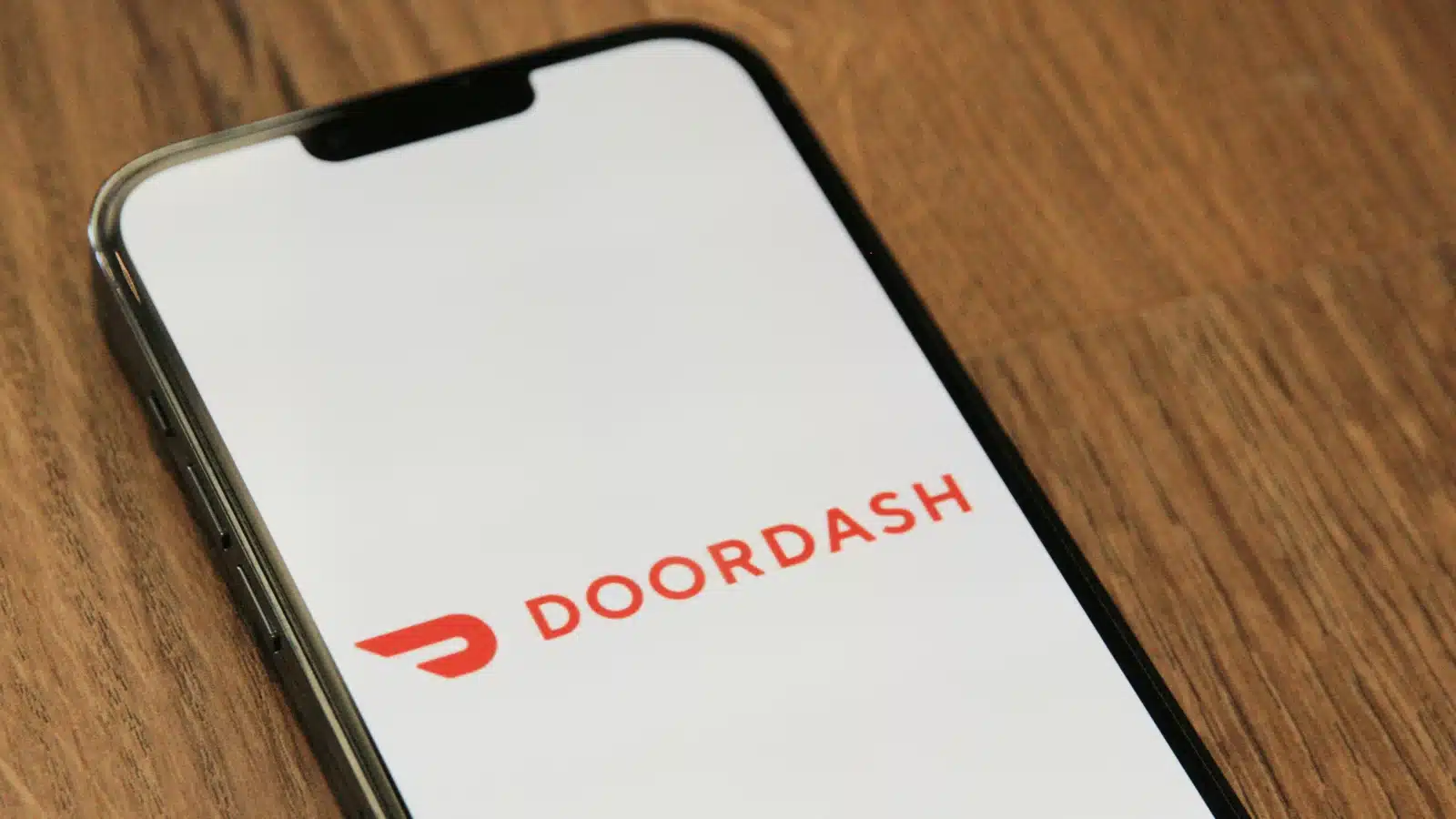 一部手机上显示着DoorDash外卖平台的标志,手机放置在木质桌面上。
