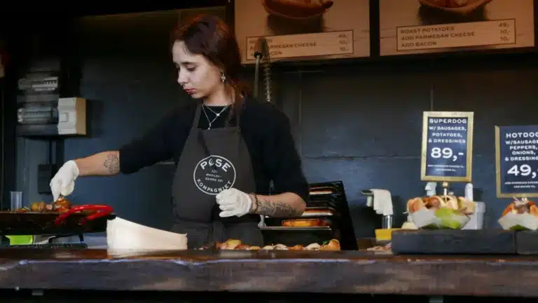 餐厅的服务人员正在准备食物,背景中展示了菜单和价格。她戴着手套,认真地进行操作,体现了餐厅对卫生和服务质量的重视。