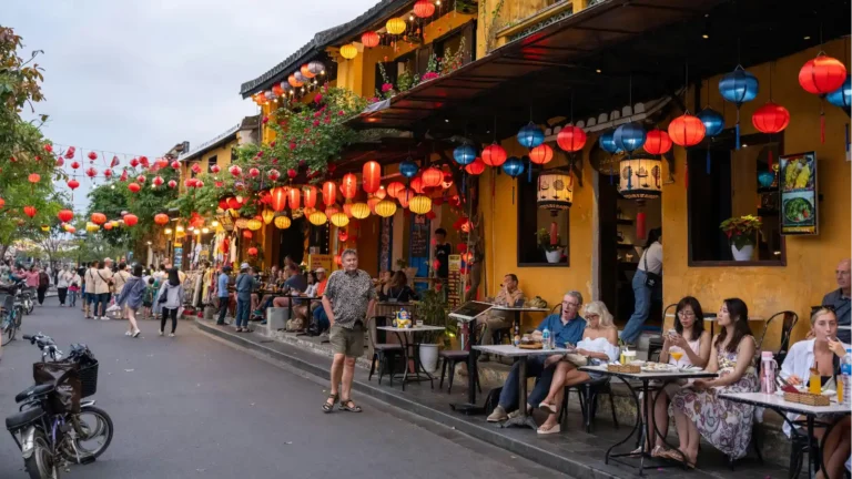 热闹的餐馆一条街，灯笼高挂，顾客在户外餐桌上享受美食并愉快交谈。