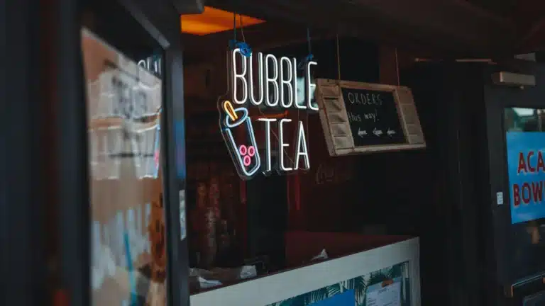 一个奶茶店的前台,挂着一个发光的“Bubble Tea”霓虹灯招牌,旁边还有一个木质的“Orders this way!”指示牌,指引顾客点单的方向。
