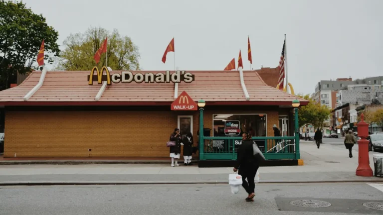 一家McDonald's门店，门口有行人走过，建筑带有标志性的红色屋顶和金色拱门形M标志