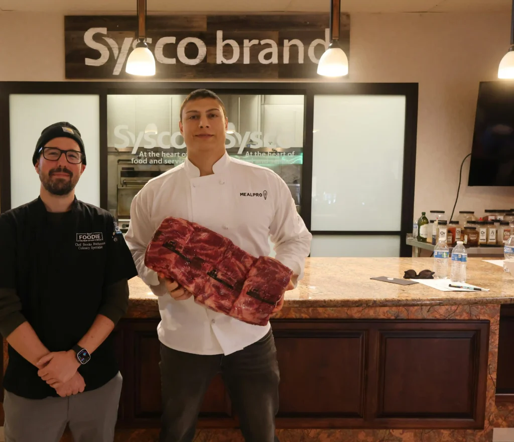 两位厨师站在Sysco展厅前，一位手持大块牛肉，展示Sysco的供应链实力