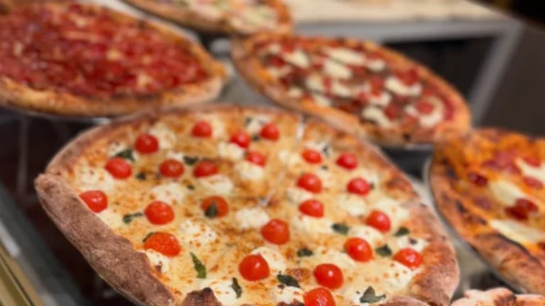 Trump Pizza橱窗内陈列着多款精致披萨，包括小番茄玛格丽特、香肠辣味、蔬菜组合等，看起来热气腾腾、色香俱全。
