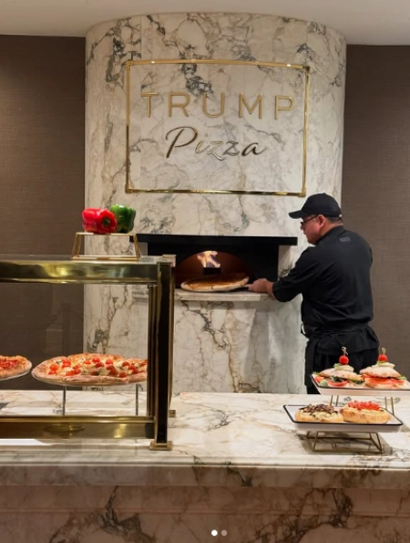 特朗普大厦新开的Trump Pizza店内，一位厨师正在金色大理石烤炉前烘烤披萨，现场展示意式手工制作过程。