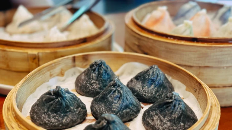 三屉不同风味的小笼包，前景为墨汁黑色皮的小笼包，后方为原味和彩色蔬菜口味，摆放在传统竹制蒸笼中。