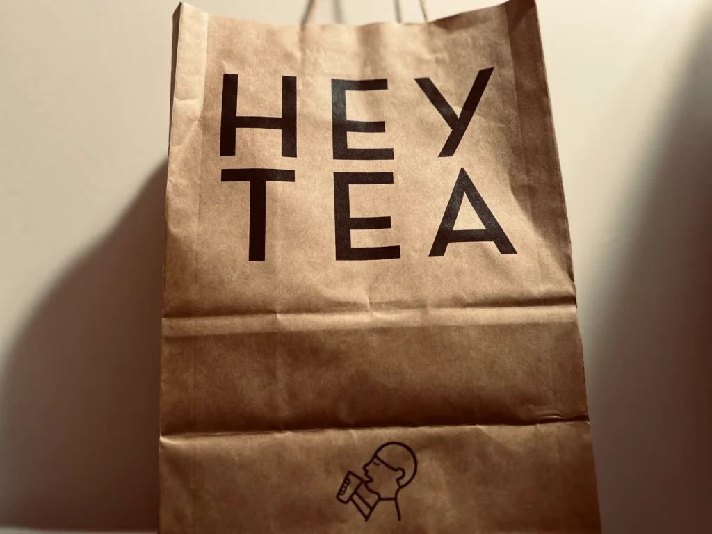 喜茶HEYTEA牛皮纸手提袋特写，黑色字样与“小人喝茶”图标清晰，突出品牌识别与外带包装。