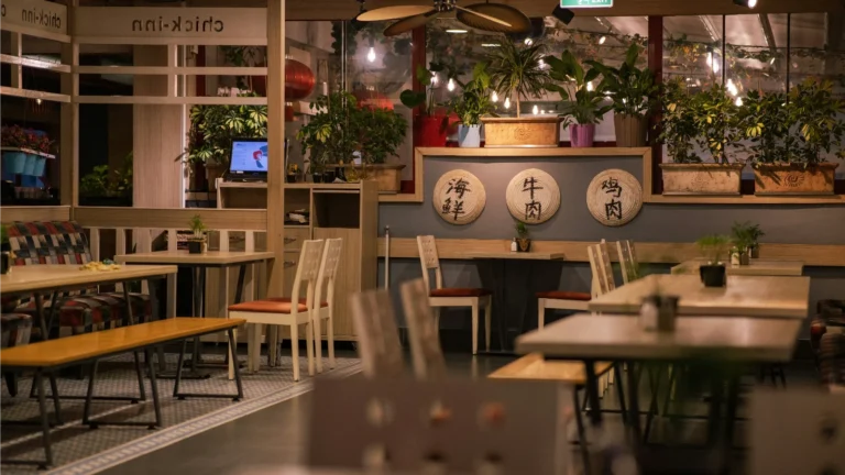 现代风格的亚洲餐厅内部，摆放着木质餐桌、植物装饰及墙面挂饰，环境温馨整洁，展示餐厅的日常堂食布局。