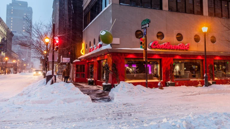 大雪覆盖的美国街角餐厅外景，街道积雪严重、行人稀少，反映寒潮对餐饮客流与营业环境的影响