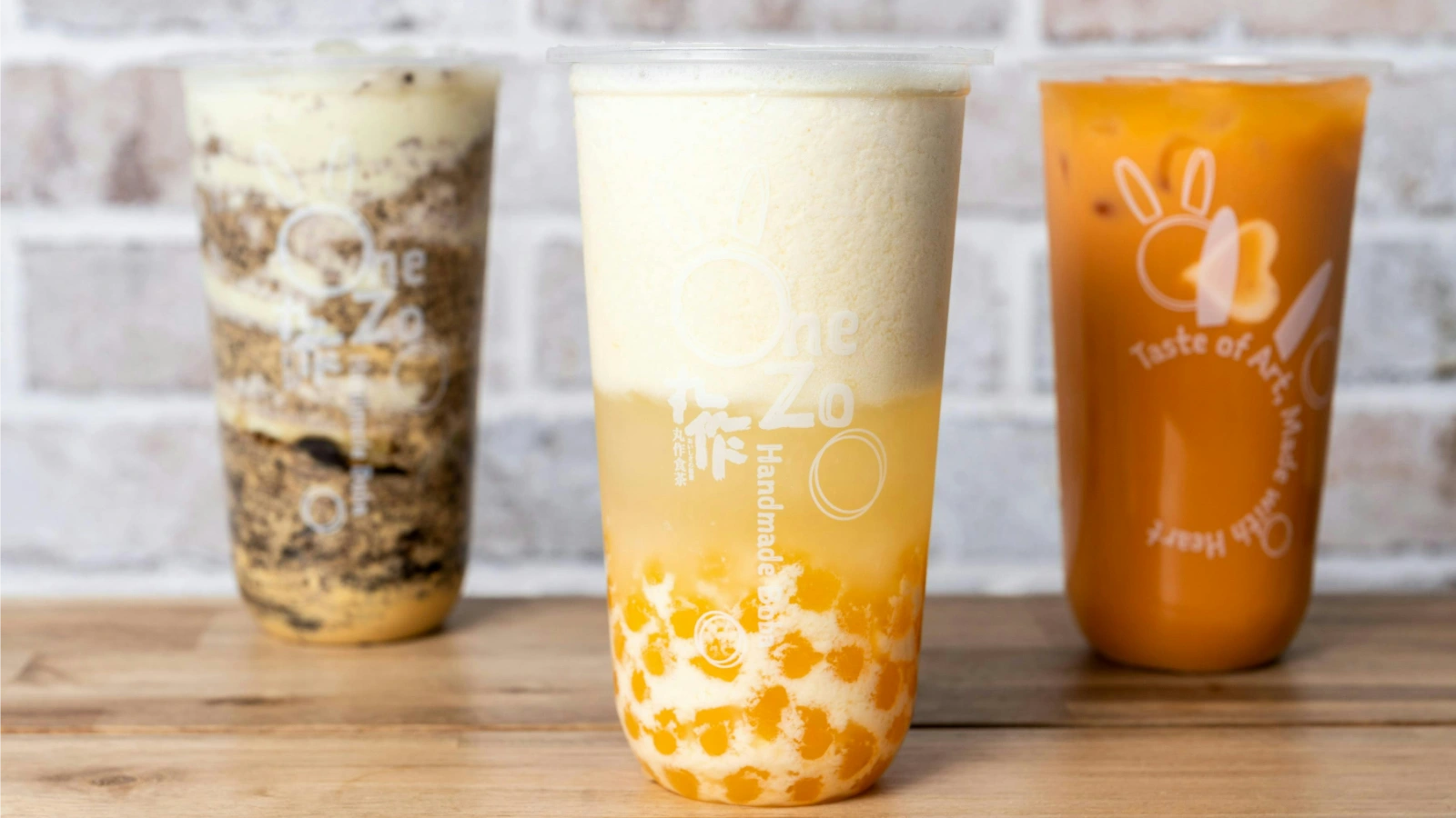 桌面上摆放的三杯奶茶饮品,中间一杯可见橙色爆爆珠与奶盖,体现美国奶茶市场中的产品创新趋势