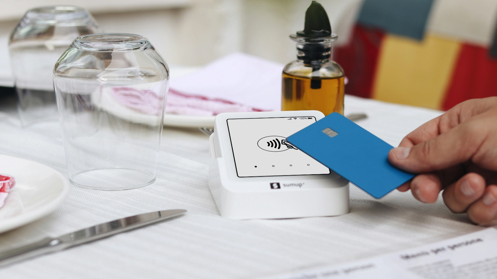 顾客在餐桌旁使用银行卡进行非接触式支付,刷卡设备放置在桌面上,体现便捷结账体验。