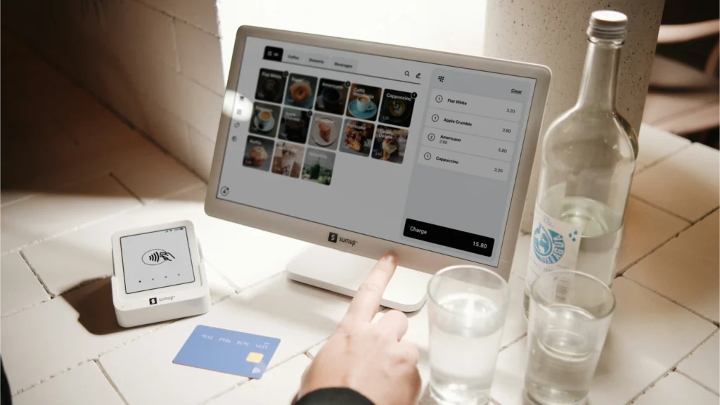 餐厅柜台上的POS收银设备与非接触式刷卡器,旁边摆放水杯和瓶装水,展示现代支付环境。