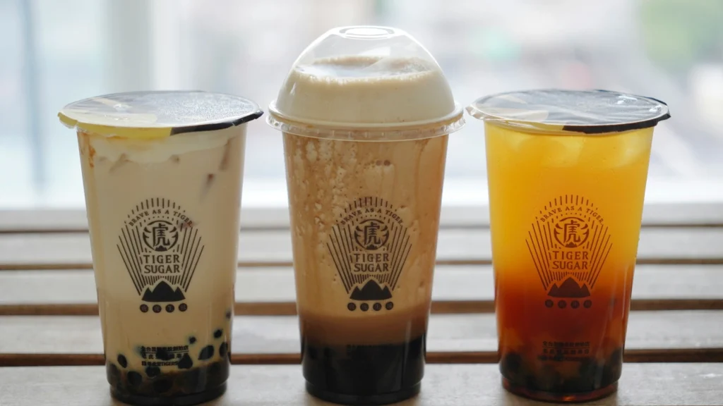 奶茶饮品展示图,三杯不同口味的珍珠奶茶摆放在窗边木桌上
