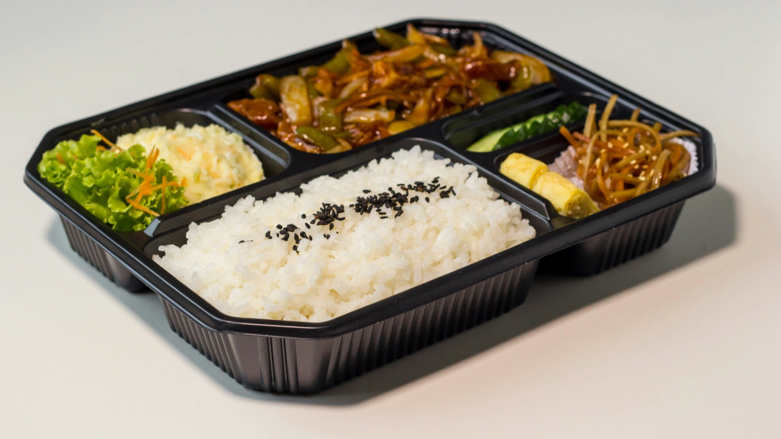 黑色分格外卖餐盒中装有米饭、配菜和主菜,展示美国餐馆外卖包装、餐品呈现与运营成本控制场景。