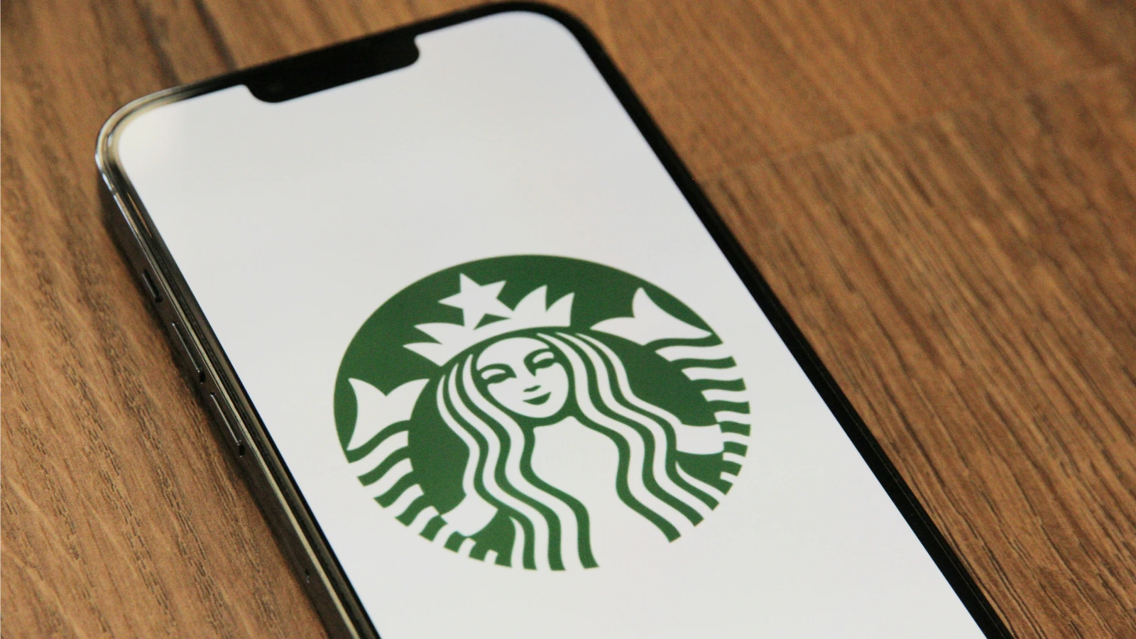 手机屏幕上显示 Starbucks 标志,展示星巴克通过移动应用承接数字点餐、会员运营和订单转化的场景。