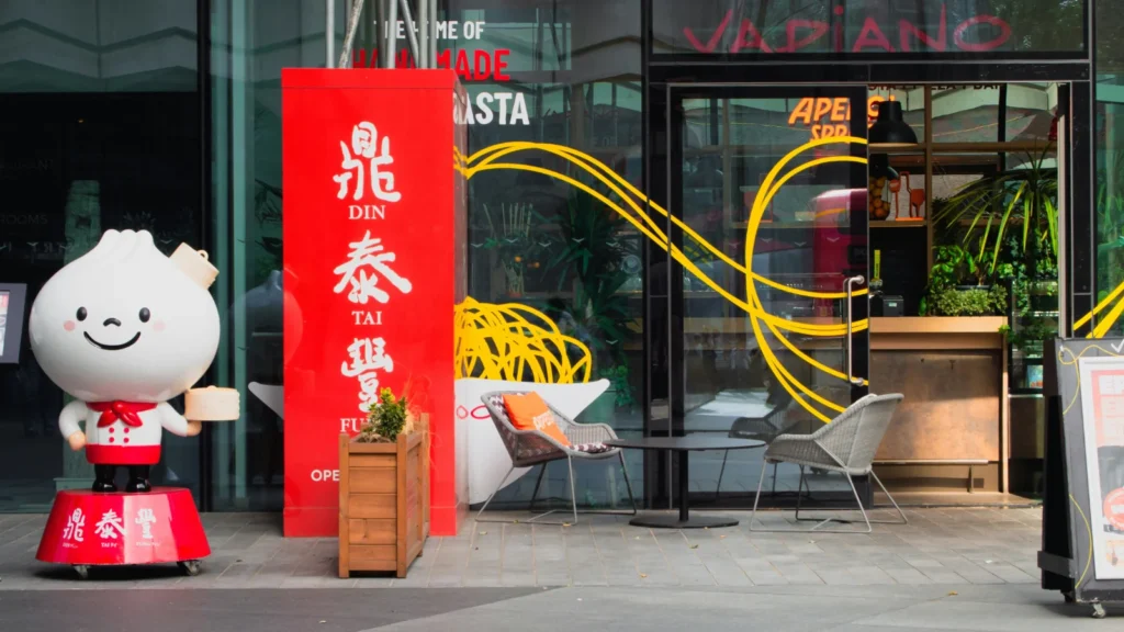 鼎泰丰Din Tai Fung餐厅外观,门前设有红色鼎泰丰品牌立柱和小笼包卡通形象,展示知名台湾餐饮品牌的门店形象与商业空间设计。